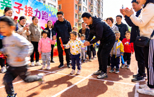社区亲子运动会上家长与孩子一起参与接力跑，现场气氛热闹