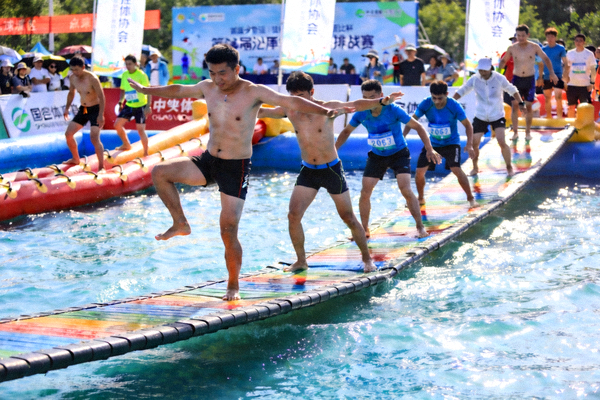 水上趣味挑战赛现场，参与者在充气浮桥上完成平衡类趣味项目